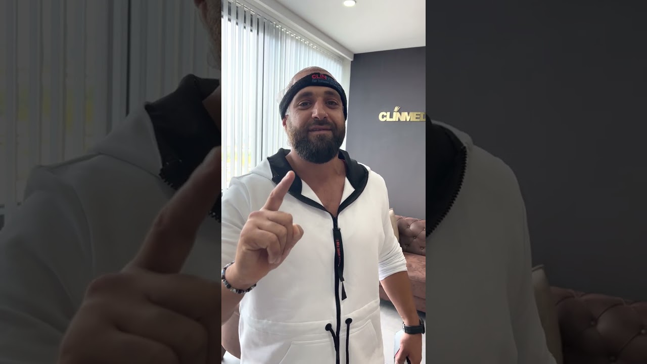 ClinMedica saç bandı ve beyaz fermuarlı kapüşonlu giyen, bir parmağını kaldırmış bir erkek; arkasındaki duvarda altın rengi ClinMedica harfleri